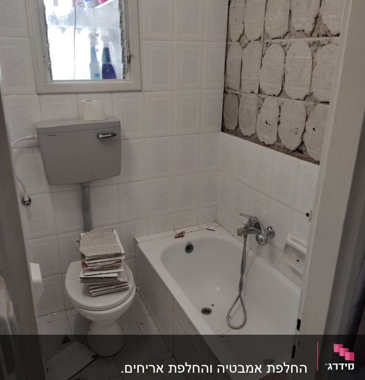 חדר אמבטיה בשיפוץ עם אריחים שבורים וקיר חשוף